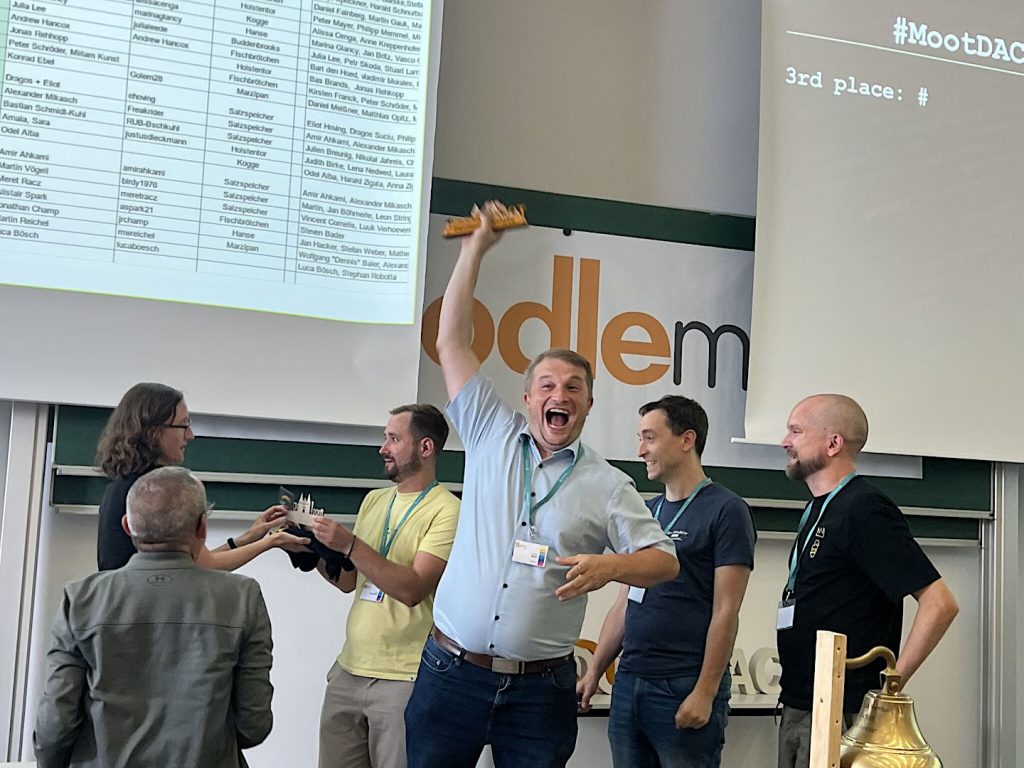 Peter Mayer freut sich mit seinem Team "AI Agents" mit MoodleMoot DACH 2025 Präsent in der rechten Hand emporgehoben